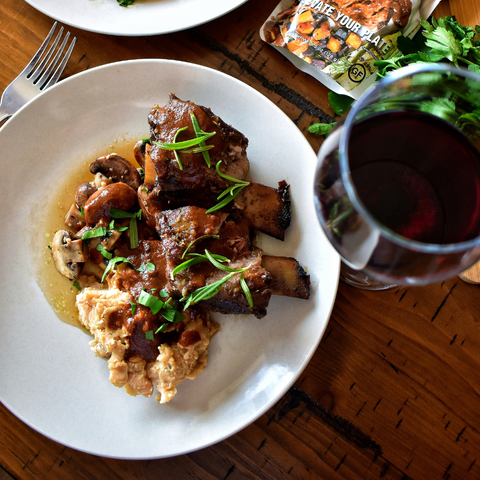 Classic Braised Beef Short Ribs over White Bean Mash and Sautéed Mushrooms finished with Mole Sauce and Fresh Herbs