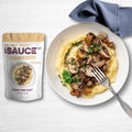 Packaging of gourmet gravy mix with a prepared dish of mushrooms over polenta, garnished with parsley, on a white plate with a fork and a blue napkin on the side.